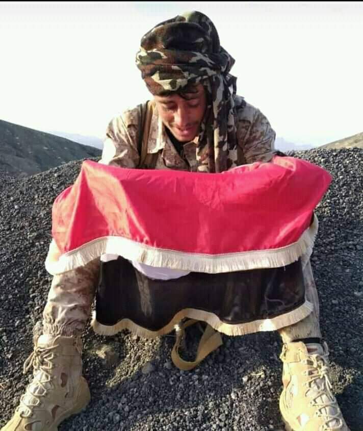من قمة جبال هيلان ..جندي يمني يُقبّل علم بلاده  والدموع تنهمر من عينيه.. صورة